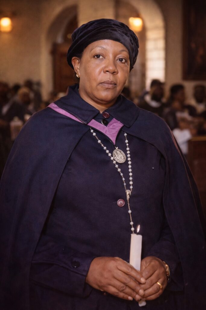 Grandmother Hanke standing in a Catholic church holding a candle, representing faith, wisdom and generational guidance in a South African village.