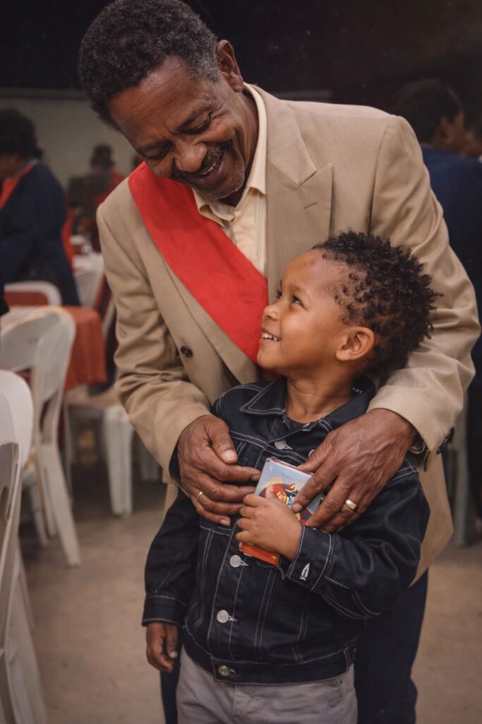 Young boy standing with his grandfather at a church gathering, sharing a warm and joyful moment together.