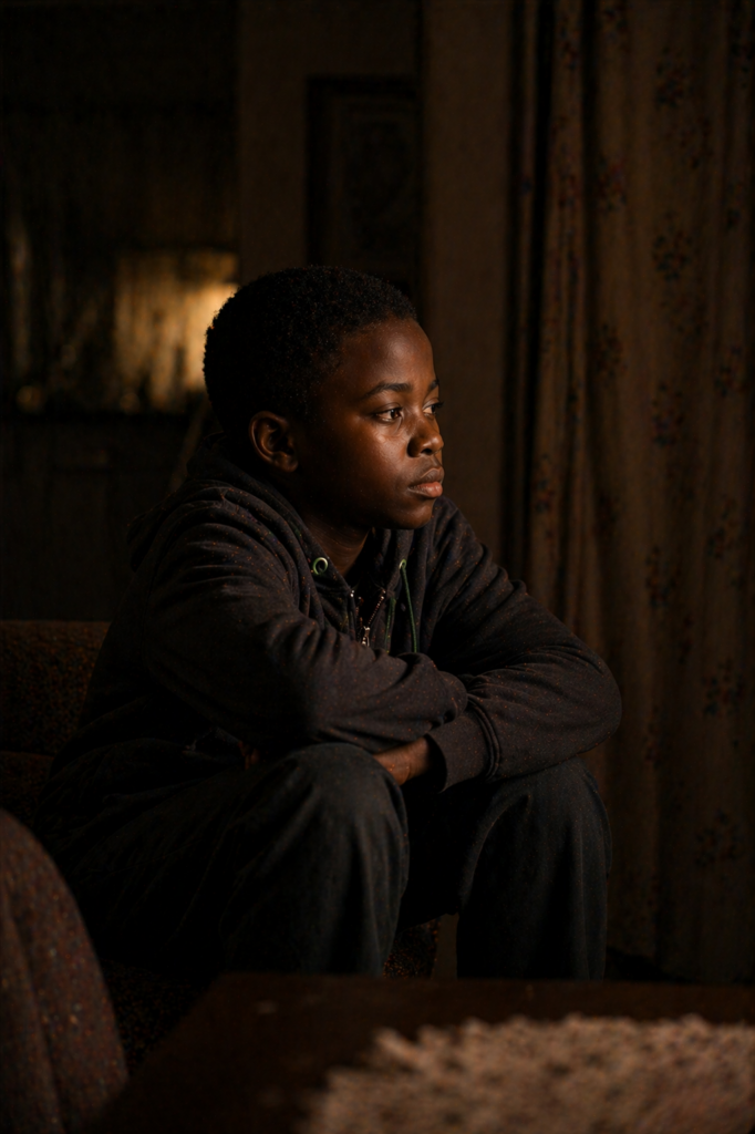 The House Where Roles Lived: young child sitting alone observing family dynamics quietly in a dimly lit room